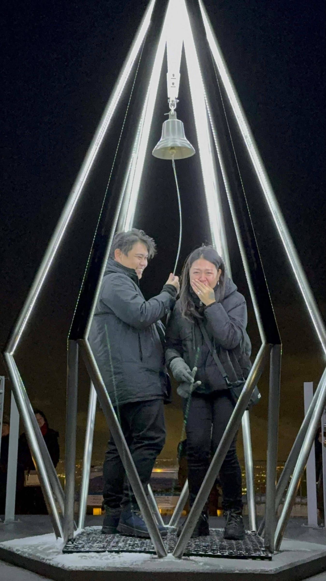 Joboy rings the bell while Anna covers her mouth, ring on her finger