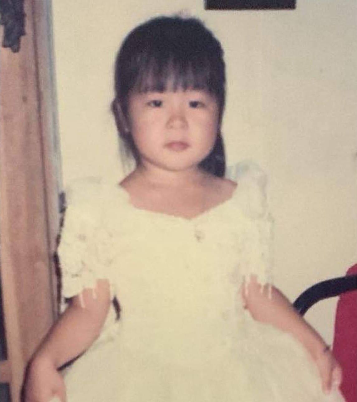 Then: Anna as a little girl with straight bangs, standing in a pale yellow party dress with ruffled sleeves.